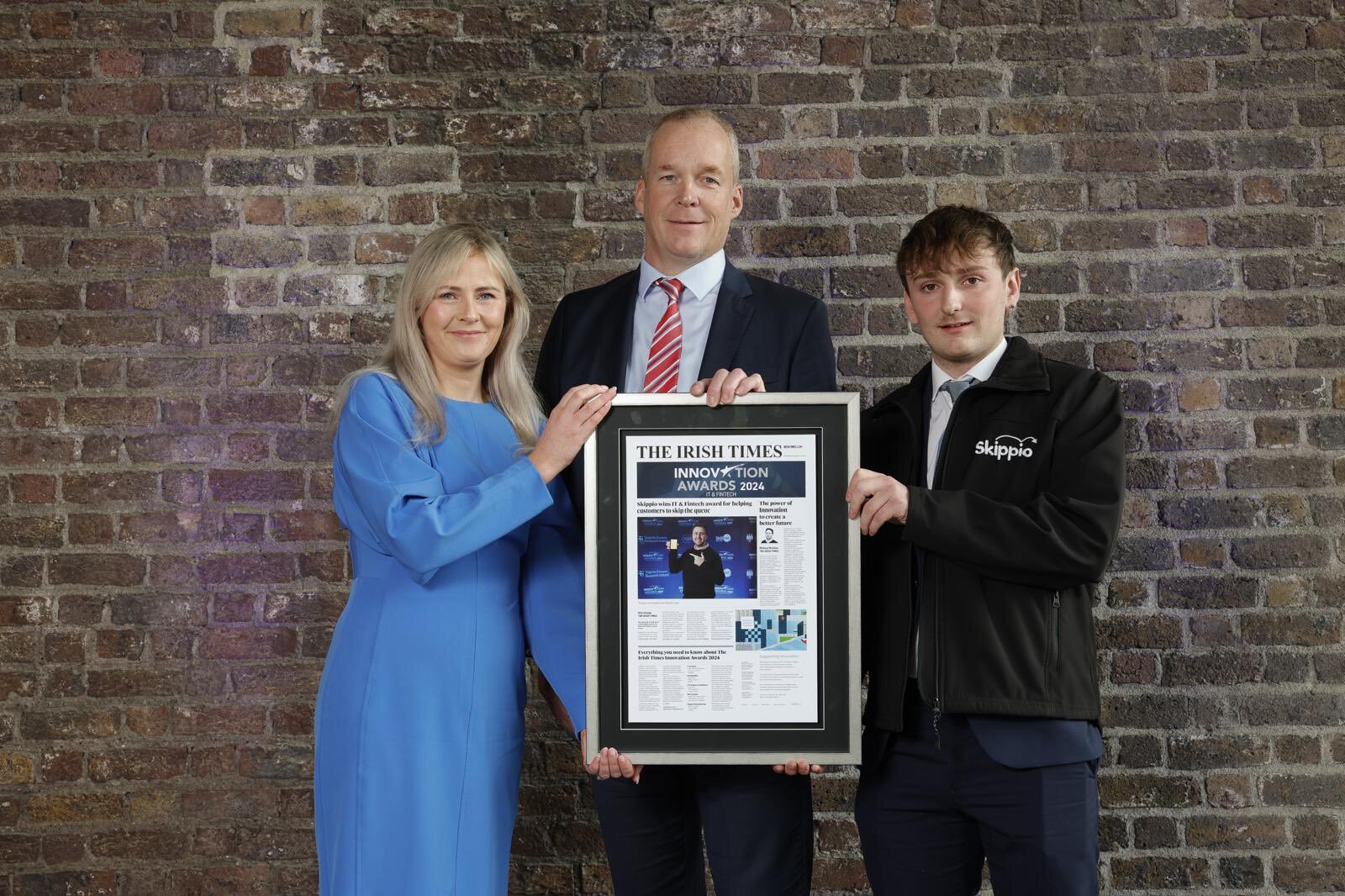 A smiling woman in a blue dress presenting an award to two men