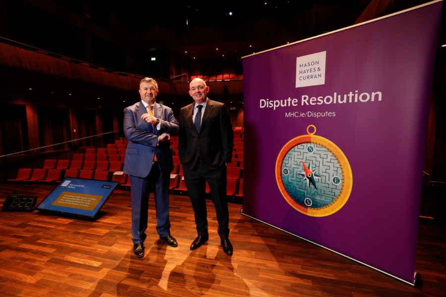 Two smiling men in business attire standing on a conference stage