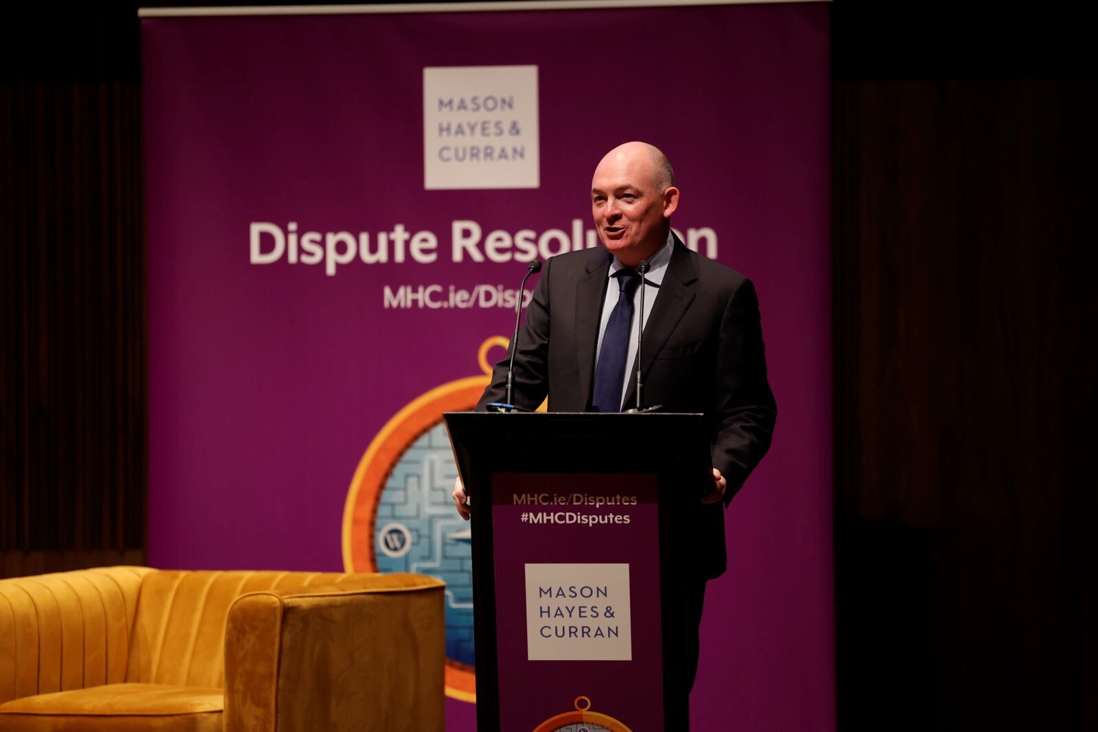 A man in business attire speaking from a podium on stage